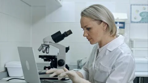 Scientist or student using laptop computer and microscope Stock Photos