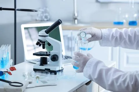 Scientist pouring blue liquid into beaker in laboratory Stock Photos