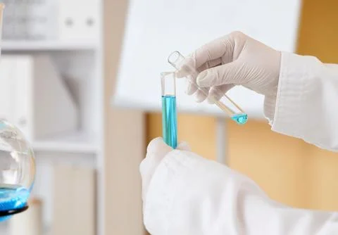 Scientist pouring blue liquid between test tubes in lab Stock Photos