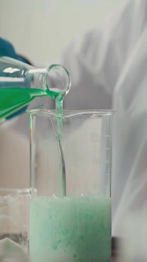 Scientist pouring green liquid into bubbling beaker in lab Video stock 331775006