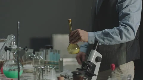 Scientist pouring liquid into petri dish with microscope and glassware nearby Stock Footage 336232801