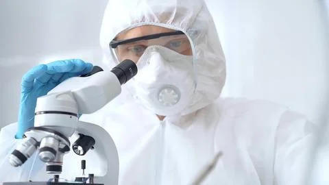 Scientist in ppe analyzing samples using a microscope in a laboratory setting 스톡 사진