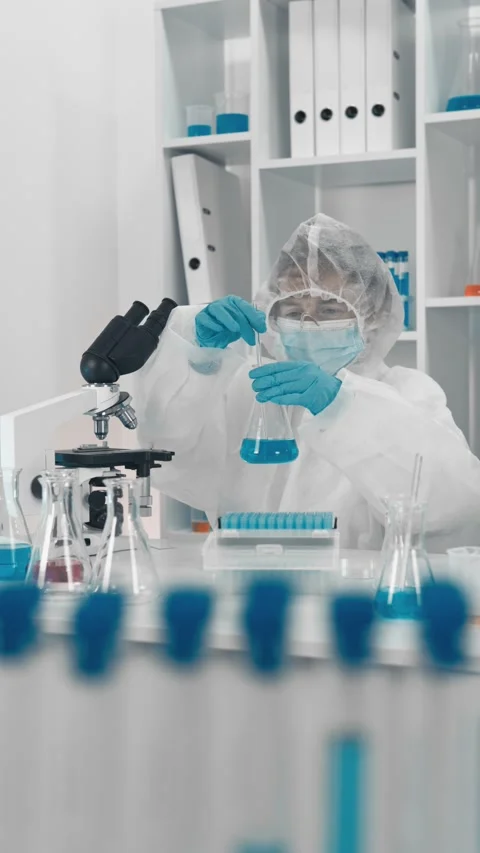 Scientist in protective suit and mask conducts chemical experiment with blue Stock Footage 340923596