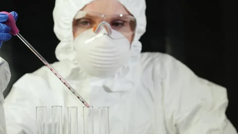 Scientist in protective suit carefully adds pink liquid drops to test tubes.. Stock Footage 334646182