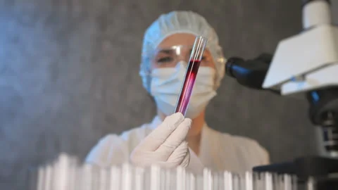 A scientist in a protective suit holds a test tube with a sample. Video stock 302172925