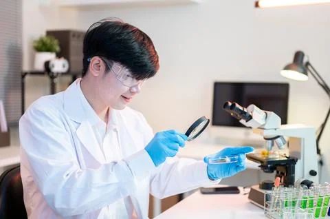 Scientist researcher man using magnifying glass look at test sample on dish.. Stock Photos