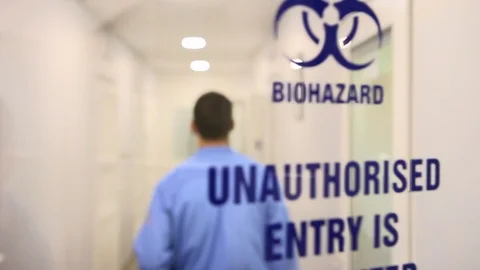 Scientist in robe open glass door with biohazard caution sign, leading to lab Stock Footage