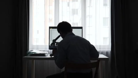 Scientist silhouette working at a desk with microscope and computer, conducting Stock Footage 346250321