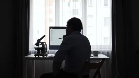 Scientist silhouette working on a desktop computer with a microscope on the Stock Footage 345531962
