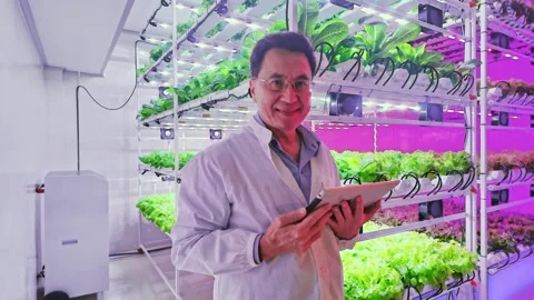 Scientist smiling while using tablet inside a vertical farming lab. 動画素材 314370858