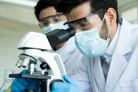 Scientist team providing protection using microscope in laboratory. Stock Photos