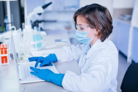 Scientist typing into the computer wearing all the safety wear. Stock Photos