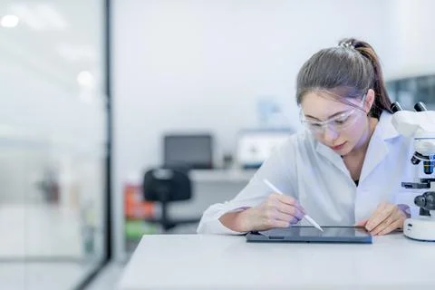 Scientist uses tablet while working in laboratory with microscope during da.. Stock Photos