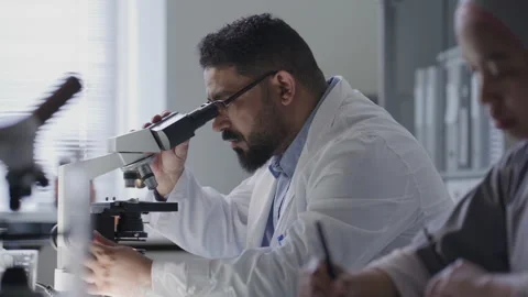 Scientist Using Microscope and Taking Notes next to Female Colleague in Lab Stock Footage 312473198