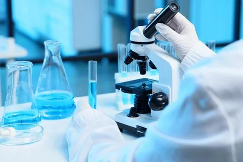Scientist using microscope with blue liquid samples in laboratory Stock Photos