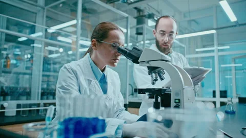 Scientist Using Microscope as Colleague Recording Data during Lab Research Stock Footage 331337640