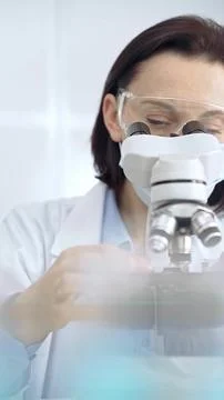 Scientist using microscope in laboratory. Focus on a woman in lab goggles Stock-Fotos
