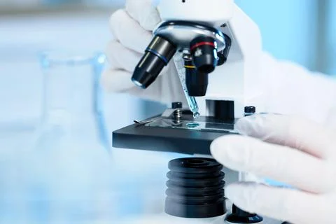 Scientist using microscope with liquid drop on slide Stock Photos