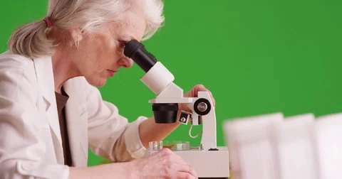 Scientist in white lab coat examining substance using microscope on greenscreen Video stock 79414017