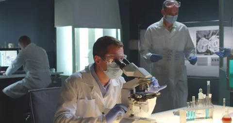 Scientist in white robe use microscope to study sample. Biologists work on Stock Footage 123994479