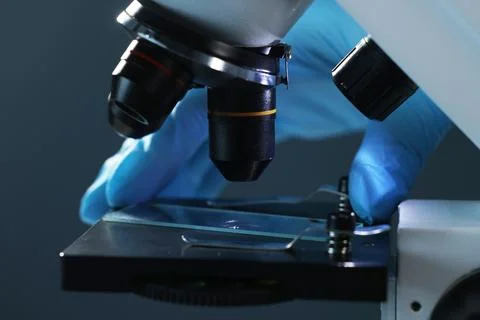 Scientist working with microscope on dark background, closeup Stock Photos