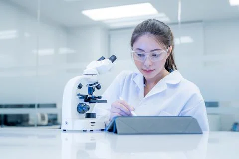 Scientist works with a tablet and microscope in a bright laboratory setting.. Stock Photos