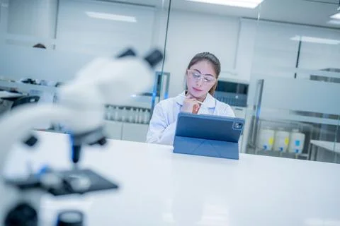 Scientist works on tablet in laboratory setting with microscope in foreground Stock Photos