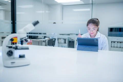 Scientist works on tablet in laboratory while using microscope and taking n.. Fotos Stock