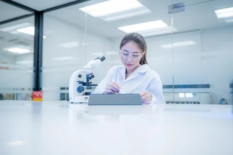 Scientist writes notes while working with a microscope in a modern laborato.. Stock Photos