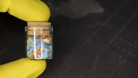 Scientist in yellow gloves holding a small glass vial with microplastics. 스톡 사진