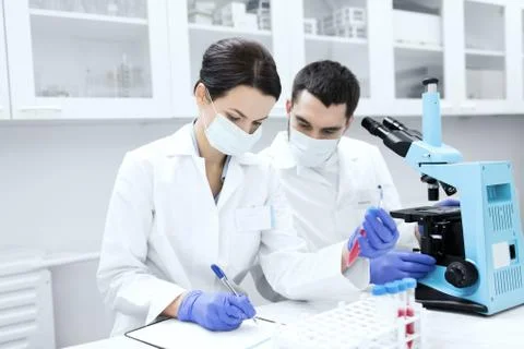 Scientists with clipboard and microscope in lab Stock Photos