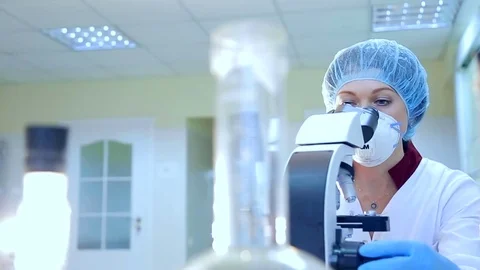 Scientists in mask looking through a microscope in a laboratory Stock Footage 72309006