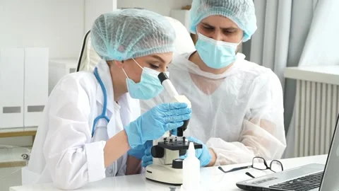 Scientists in masks explore virus covid-19 under microscope in laboratory. Stock Footage 149573034