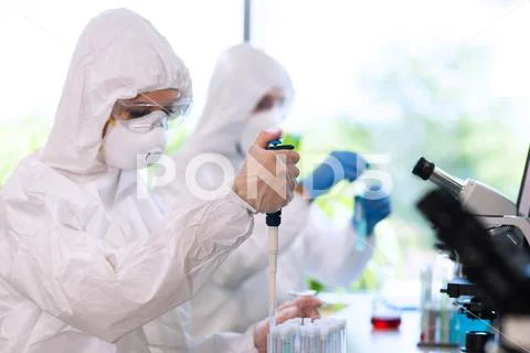 Scientists in protection suits and masks working in research lab using Stock Photos