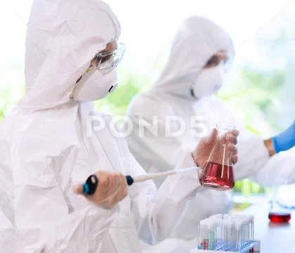 Scientists in protection suits and masks working in research lab using Stock Photos