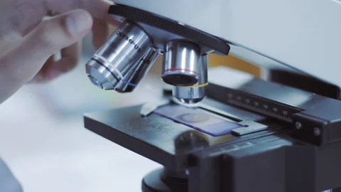 Scientists to rotate the lens of a microscope with slide Stock Footage 130122100