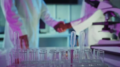 Scientists shaking hands in laboratory with test tubes in foreground Stock Footage 306584560
