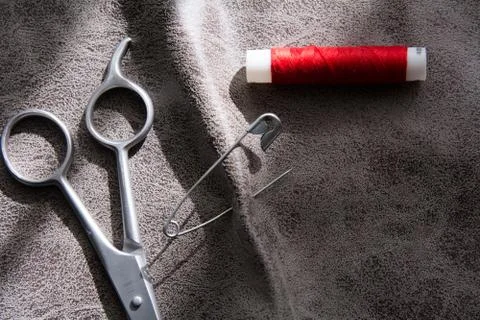 Scissors and reel of red thread on gray fabric Stock Photos