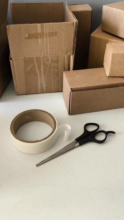 Scissors and tape on the table against the background of boxes. Warehouse 库存影片 330040106