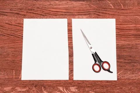Scissors and a white sheet cut in half. Background of pinkish brown wood. Stock Photos
