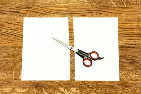 Scissors and a white sheet cut in half. Background yellowish brown wood. Stock Photos