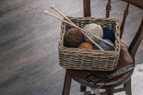 Scissors and yarn inside old basket on wooden chair 스톡 사진