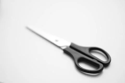 Scissors with a black handle are on the white surface. Stock Photos