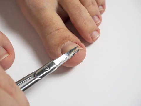 Scissors cut the nails on the big toe of a woman's foot. The concept of the c Stock Photos