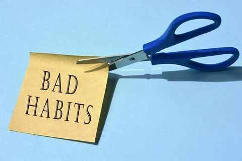Scissors that cut yellow notepad with bad habits text on a blue background. Stock Photos
