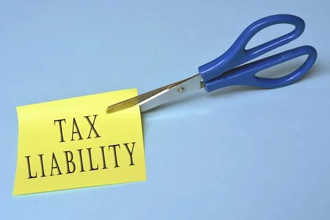 Scissors that cut yellow notepad with tax liability text Stock Photos