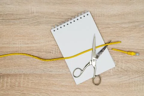 Scissors cutting data cable over a blank spiral notebook Foto stock