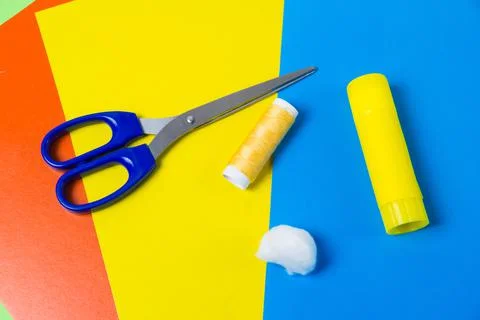 Scissors, glue, cotton wool and threads on multi-colored sheets of cardboard. Stock Photos