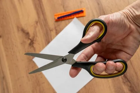 Scissors held in hand above a piece of paper on a wooden table with colorfu.. Stock Photos