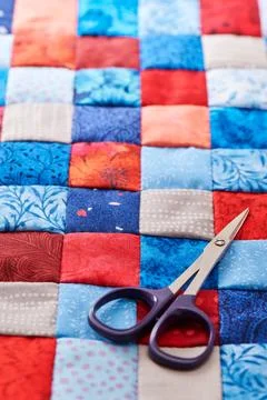 Scissors lying on blue and red square pieces of fabric sewn together Stock-Fotos